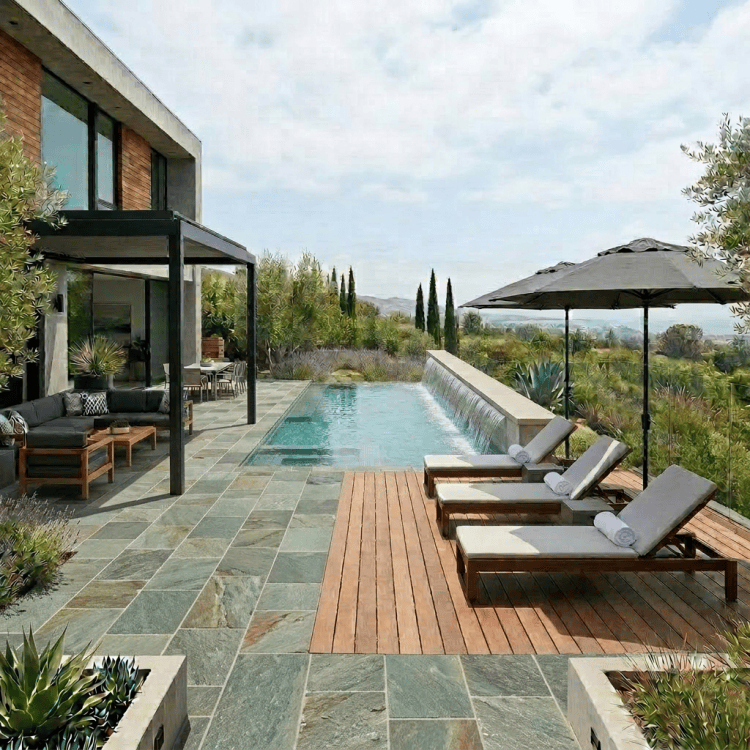 Rectangular swimming pool with swimmer, lounge chairs, shaded seating area, and waterfall feature